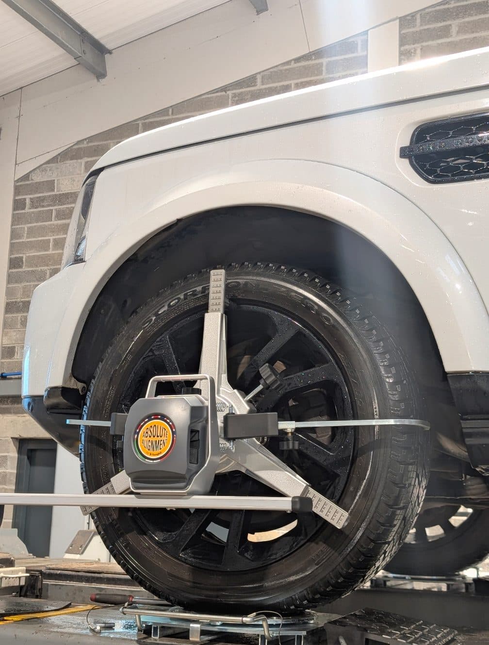 A wheel alignment sensor clamped to a Land Rover wheel on the alignment ramp